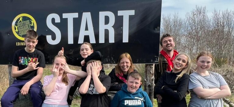A group of young people pose in front of a large "START" sign post